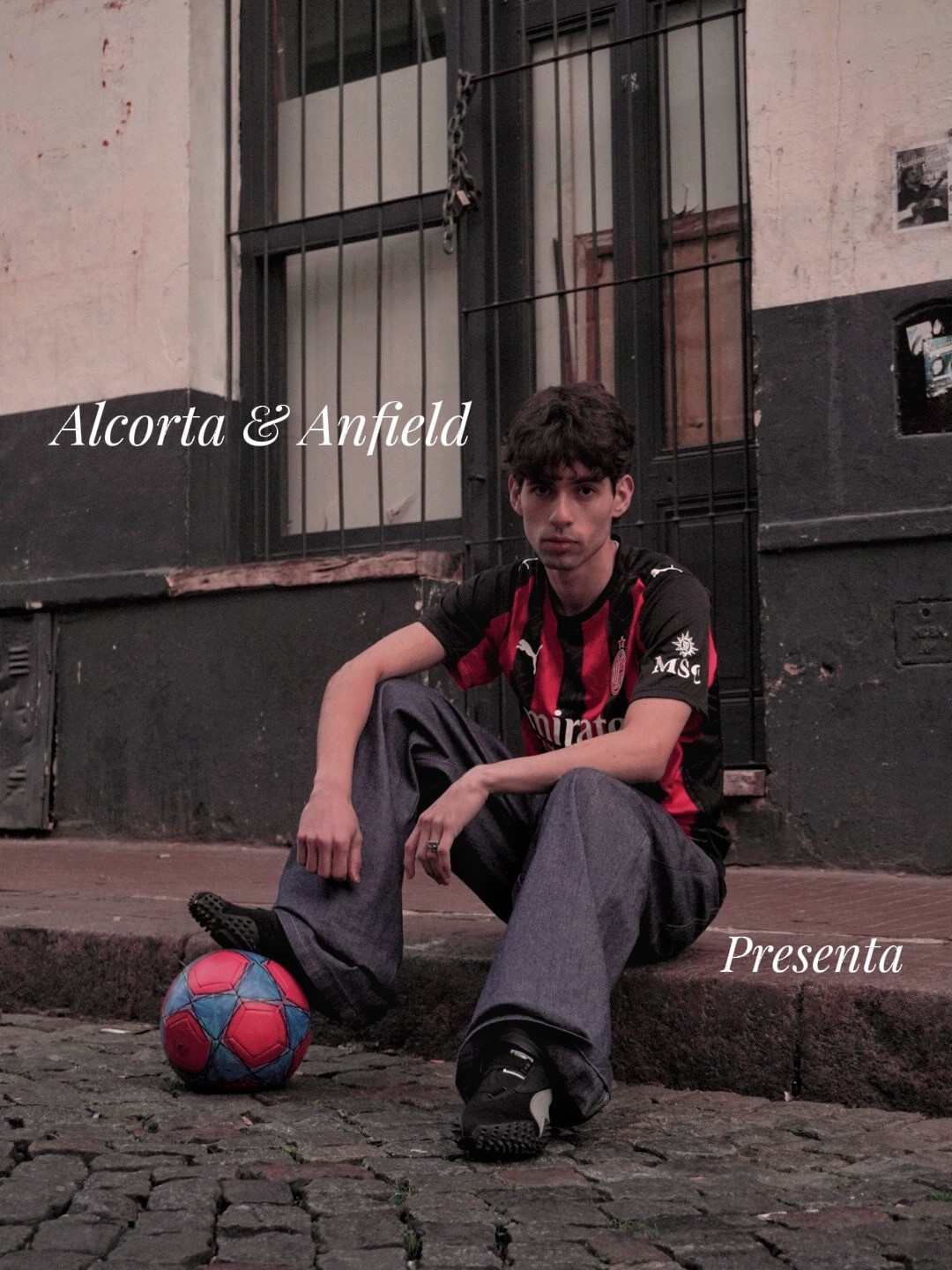 Persona con camiseta roja y negra junto a una pelota frente a una pared